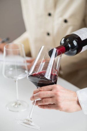 Téléchargez les photos : Expérience de dégustation de vin. Un sommelier verse du vin rouge d'une bouteille dans un verre à vin, démontrant la technique appropriée pour servir du vin aux invités. - en image libre de droit
