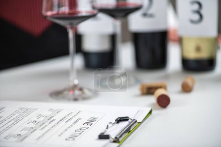 Téléchargez les photos : Formulaire de dégustation de vin avec verres et bouteilles de vin rouge en arrière-plan - en image libre de droit