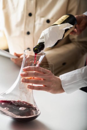 Photo for Decanting wine. A sommelier pours red wine from a bottle into a decanter, while explaining how to aerate wine to improve its flavor and aroma. - Royalty Free Image