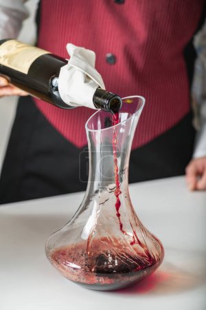 Foto de Vino decantante. Un sommelier vierte vino tinto de una botella en un decantador, mientras explica cómo airear el vino para mejorar su sabor y aroma. - Imagen libre de derechos