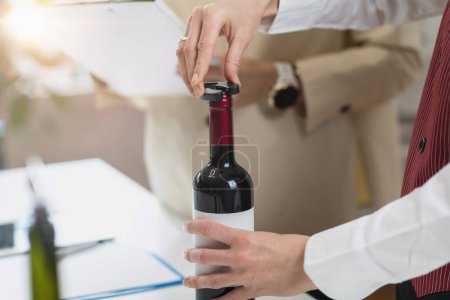 Foto de Experiencia de cata de vinos. El sommelier retira la lámina que cubre la parte superior de una botella de vino, mientras explica la manera correcta de preparar una botella de vino para el servicio. - Imagen libre de derechos