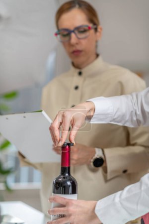 Foto de Experiencia de cata de vinos. El sommelier retira la lámina que cubre la parte superior de una botella de vino, mientras explica la manera correcta de preparar una botella de vino para el servicio. - Imagen libre de derechos