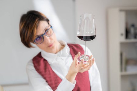 Foto de Sommelier sostiene una copa de vino y evalúa la apariencia de un vino tinto, mirando su color, claridad y viscosidad. - Imagen libre de derechos