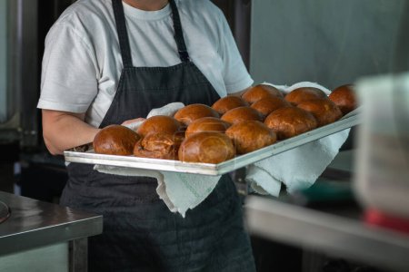 Photo for Baker taking baked buns out of the oven in restaurant kitchen - Royalty Free Image