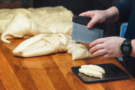 Téléchargez les photos : Boulanger couper et peser la pâte dans une cuisine de restaurant - en image libre de droit