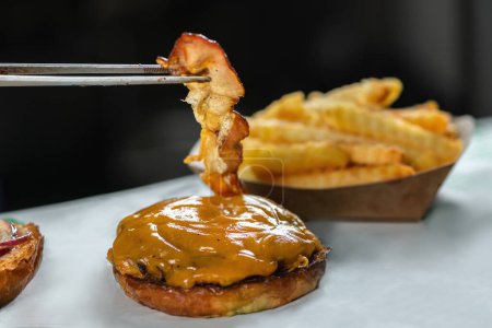 Téléchargez les photos : Chef restaurant plaçant une tranche de bacon croustillant à un sandwich cheeseburger, fermer - en image libre de droit