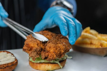 Photo for Preparation of crispy fried chicken. Restaurant chef placing piece of crispy fried chicken onto the bun. - Royalty Free Image