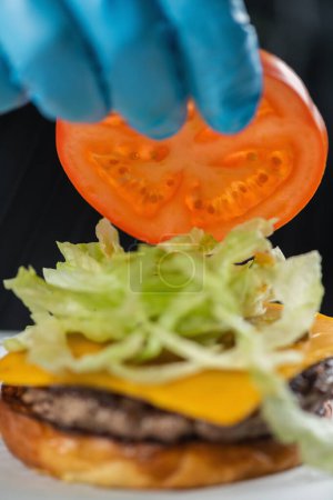 Téléchargez les photos : Chefs main plaçant tranche de tomate à un hamburger dans un restaurant - en image libre de droit