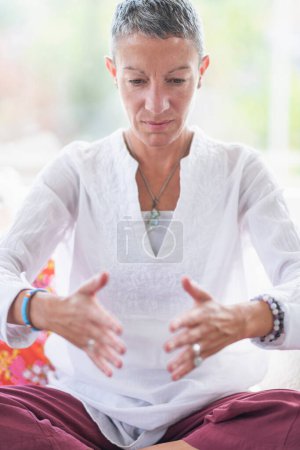 Foto de Mujer consciente practicando meditación de enfoque en casa. Señora de mediana edad tranquila sentada en pose de loto meditando para un mejor enfoque - Imagen libre de derechos