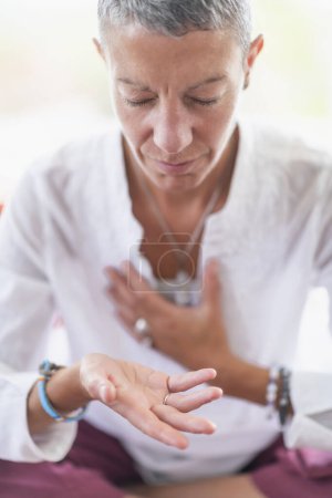 Foto de Mujer consciente sentada en posición de loto, meditando, realizando un gesto de respeto con las manos. Despertar espiritualmente - Imagen libre de derechos