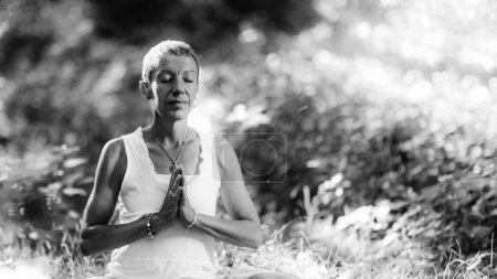 Téléchargez les photos : Méditation dans la nature Femme consciente méditant, assise par terre les mains en position de prière, les yeux fermés, embrassant les aspects positifs de la nature, se baignant dans la lumière du soleil - en image libre de droit