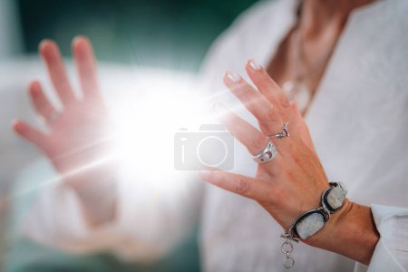 Ausstrahlung spiritueller Energie. Spirituelle Lehrerin strahlt eine leuchtende, glühende Energiekugel zwischen ihren Händen aus, die ihre tiefe spirituelle Verbundenheit und ihre Heilkraft zeigt.