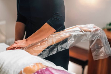 Photo for Anti-cellulite bagging vacuum therapy for arms and legs. Female client lying on a massage table in a beauty wellness center, arms and legs in a nylon bag. - Royalty Free Image