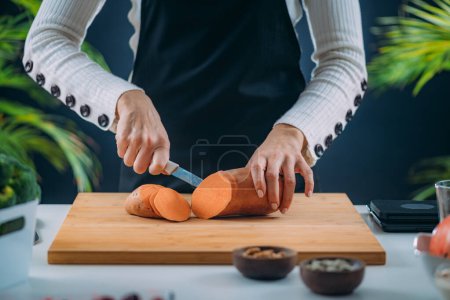 Foto de Mujer Cortar la patata dulce orgánica fresca, superalimento rico en triptófano, potasio, vitamina C, fitonutrientes y fibras dietéticas - Imagen libre de derechos