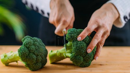 Photo for Woman Cutting fresh organic broccoli, superfood rich in vitamin K, vitamin C, folic acid, potassium, phytonutrients and fibers - Royalty Free Image