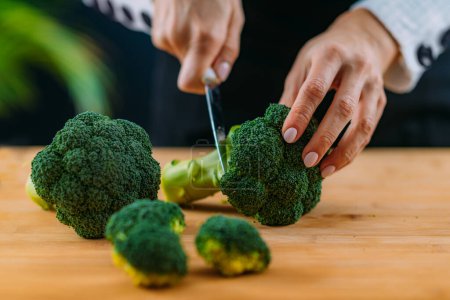 Photo for Woman Cutting fresh organic broccoli, superfood rich in vitamin K, vitamin C, folic acid, potassium, phytonutrients and fibers - Royalty Free Image