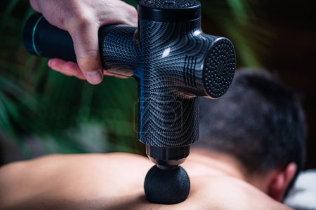 Photo for Massage Gun Physical Therapy Treatment. Physical Therapist Massaging Mans Back Muscles - Royalty Free Image