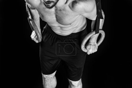 Téléchargez les photos : Jeune homme montrant sa force et son agilité à travers des exercices de cross training avec des anneaux de gymnastique, photo noir et blanc - en image libre de droit