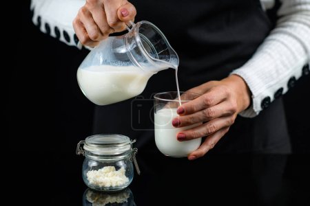 Photo for Woman Pouring homemade kefir in a glass from a jug. - Royalty Free Image
