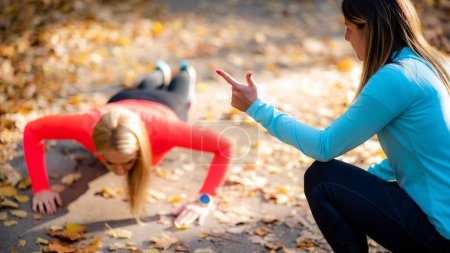 Foto de Mujer haciendo flexiones, entrenador personal de fitness contando durante el entrenamiento en el parque. - Imagen libre de derechos
