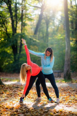 Foto de Mujer Stretching with Personal Fitness Trainer Después del entrenamiento en el parque. - Imagen libre de derechos
