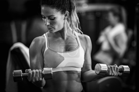 Téléchargez les photos : Athlète féminine faisant de l'exercice avec des haltères dans la salle de gym, noir et blanc - en image libre de droit