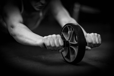Téléchargez les photos : Femme faisant de l'exercice avec Abs Roue à rouleaux dans la salle de gym, noir et blanc - en image libre de droit