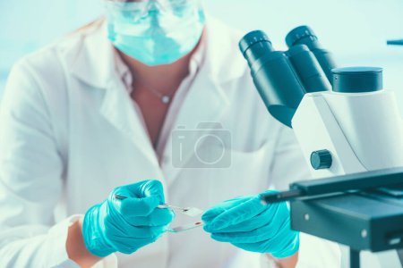 Photo for Scientist working in a laboratory, placing microscope slide on the stage - Royalty Free Image