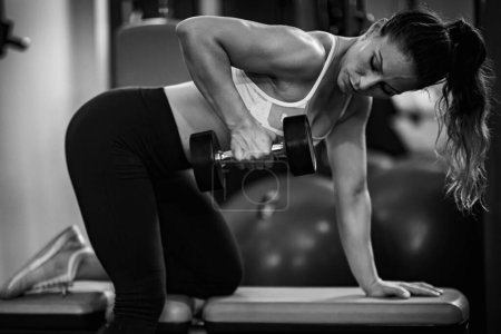 Téléchargez les photos : Femme faisant Triceps exercice de force dans une salle de gym, noir et blanc - en image libre de droit