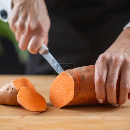 Frau schneidet Süßkartoffeln, ein Superfood reich an Tryptophan, Kalium, Vitamin C, Phytonährstoffen und Ballaststoffen