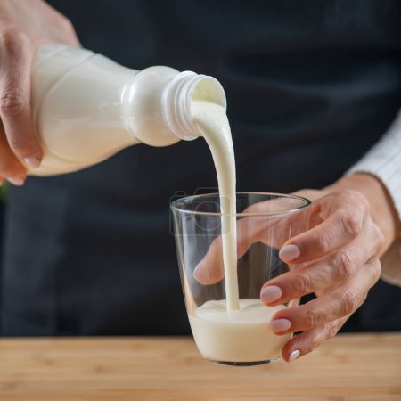 Foto de Mujer vertiendo kéfir, una bebida láctea fermentada, rebosante de probióticos naturales Lacto y Bifido Bacterium. - Imagen libre de derechos
