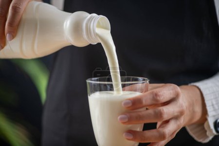 Foto de Mujer vertiendo kéfir en el vaso, una bebida láctea fermentada de superalimentos, rebosante de probióticos naturales Lacto y Bifido Bacterium. - Imagen libre de derechos