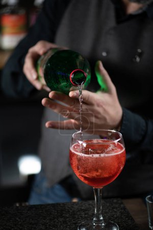 Bartender prepares a Bicicletta cocktail, pouring the sparkling water into a wine glass.