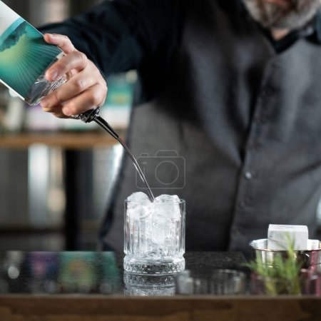Les mains du barman versant du gin, confectionnant des aromatiques gin tonic cocktail 