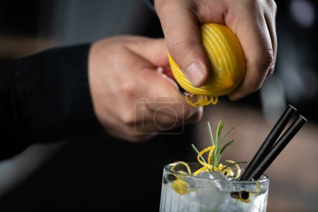 Téléchargez les photos : Les mains du barman ajoutent délicatement de la peau de citron, insufflant une saveur vibrante dans un cocktail Gin Tonic classique. - en image libre de droit