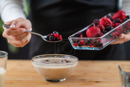 woman holding spoon full of berries and oatmeal, combining wholesome oats, creamy soy milk, and a medley of luscious berries for a vibrant and nutritious breakfast.  
