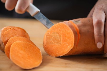 woman cutting Sweet potatoes, a superfood rich in tryptophan, potassium, vitamin C, phytonutrients, and dietary fibers
