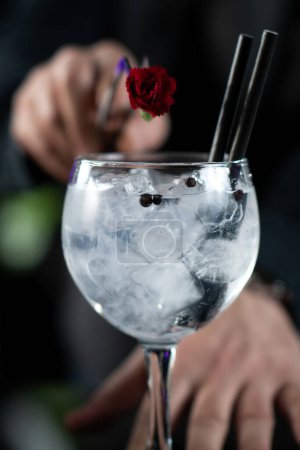 Barkeeper fügt eine zarte essbare rote Blume hinzu, die den Charme des Gin Tonic Cocktails unterstreicht.