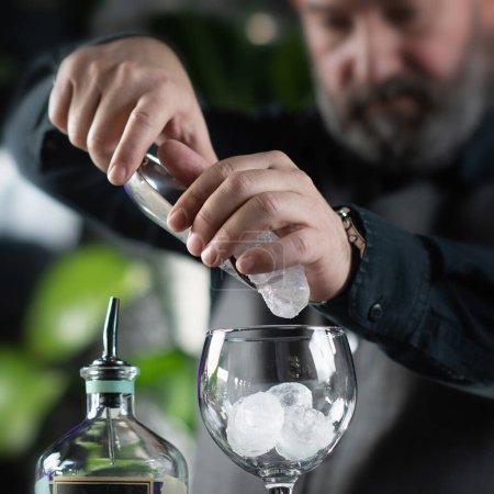 Gin tonic Cocktail Preparation - Bartender filling the glass with ice cubes.