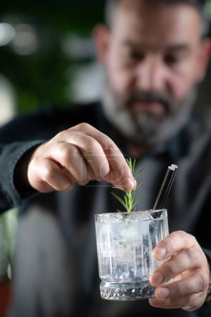Photo for Professional bartender preparing cocktails adding fresh rosemary. - Royalty Free Image