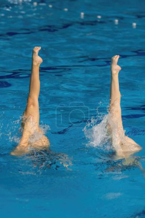 Photo for Synchronized swimming duet dance.  Synchronized swimming duet enchants the pool with their graceful dance - Royalty Free Image