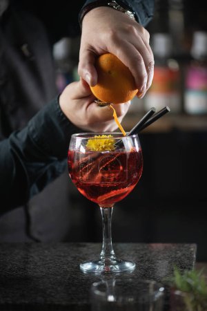 Barkeeper hebt den Bicicletta-Cocktail an und fügt gekonnt frische Orangenschalen hinzu