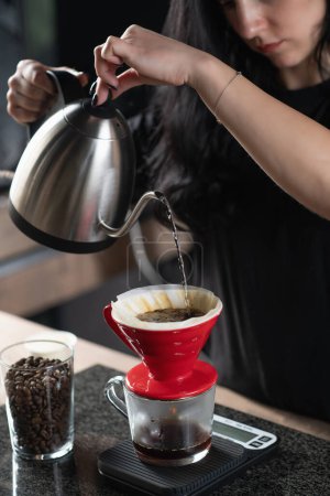 Photo for Female barista pours hot water from a kettle onto coffee grounds, creating a rich brew in a prepared filter, served in a coffee cup. - Royalty Free Image