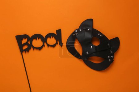 Téléchargez les photos : Masque de chat en cuir BDSM et le mot boo sur un bâton, fond orange. Fête Halloween - en image libre de droit