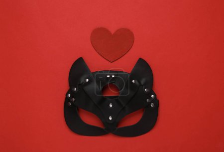 Foto de Cuero bdsm gato máscara y el corazón sobre un fondo rojo. Juego de rol sexual. Concepto de amor. Vista superior. Puesta plana - Imagen libre de derechos