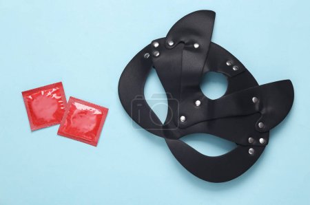 Photo for BDSM leather cat mask with condom packages on a blue background. Sex games. Top view - Royalty Free Image