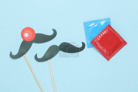 Photo for The concept of same-sex relationships. Condoms and two pairs of mustaches on sticks on a blue background - Royalty Free Image