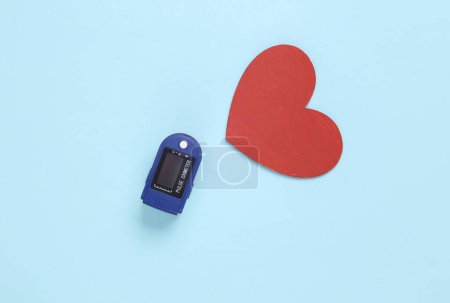 Foto de Concepto de salud. Oxímetro de pulso (un dispositivo para medir el oxígeno en la sangre) y un corazón sobre un fondo azul. Vista superior - Imagen libre de derechos