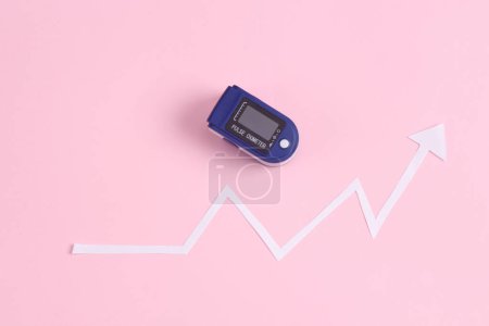 Foto de Oxímetro electrónico de pulso con flecha de crecimiento estadístico sobre fondo rosa. Estadísticas de la enfermedad de Covid 19 - Imagen libre de derechos