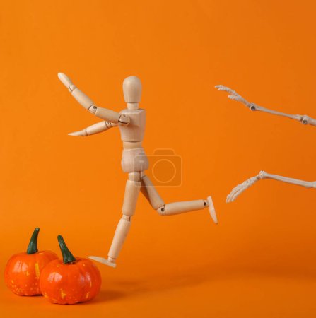 Téléchargez les photos : Le squelette poursuit une marionnette en bois sur un fond orange. Concept Halloween - en image libre de droit
